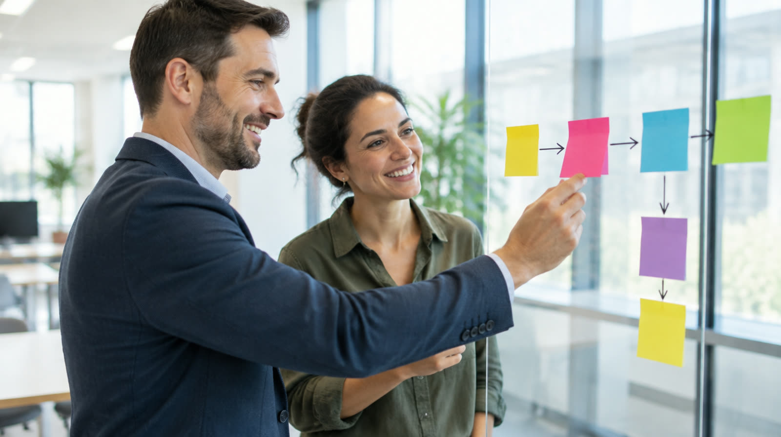 A consultant and a business owner mapping a process with sticky notes on a glass wall